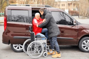 young man helping an old paralyzed man out of a van